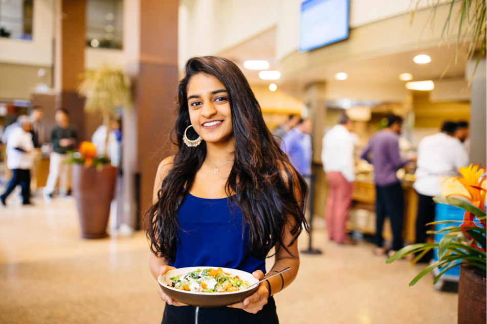 A female student holds a plate of food and poses for a picture.