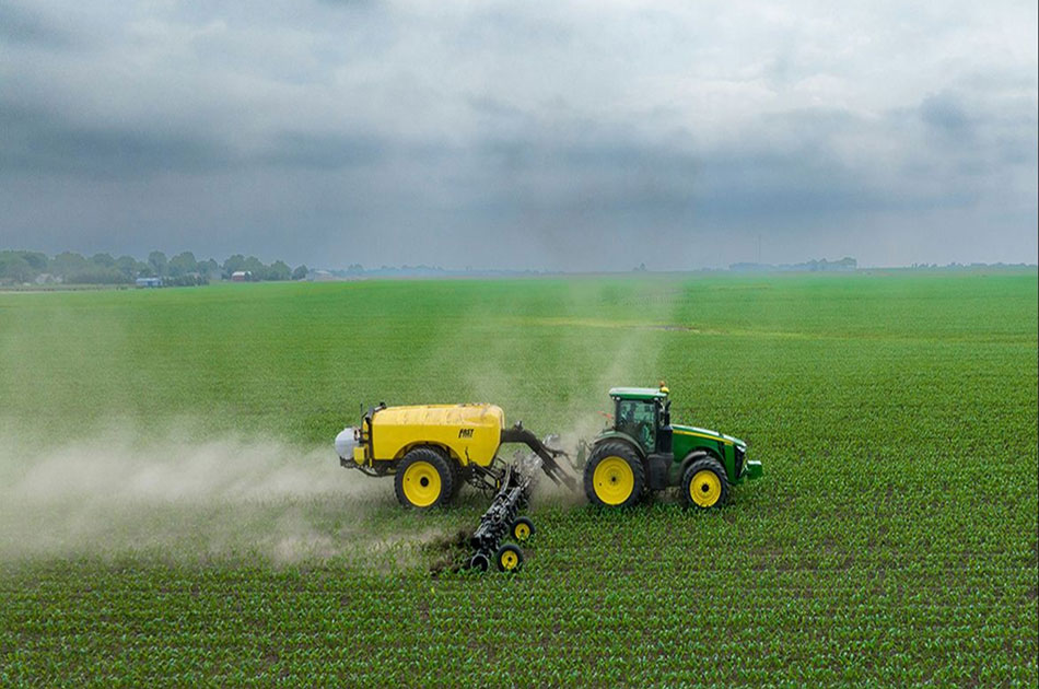 Tractor spraying pesticides on a farm with green vegetation. The sky looks cloudy and gray.