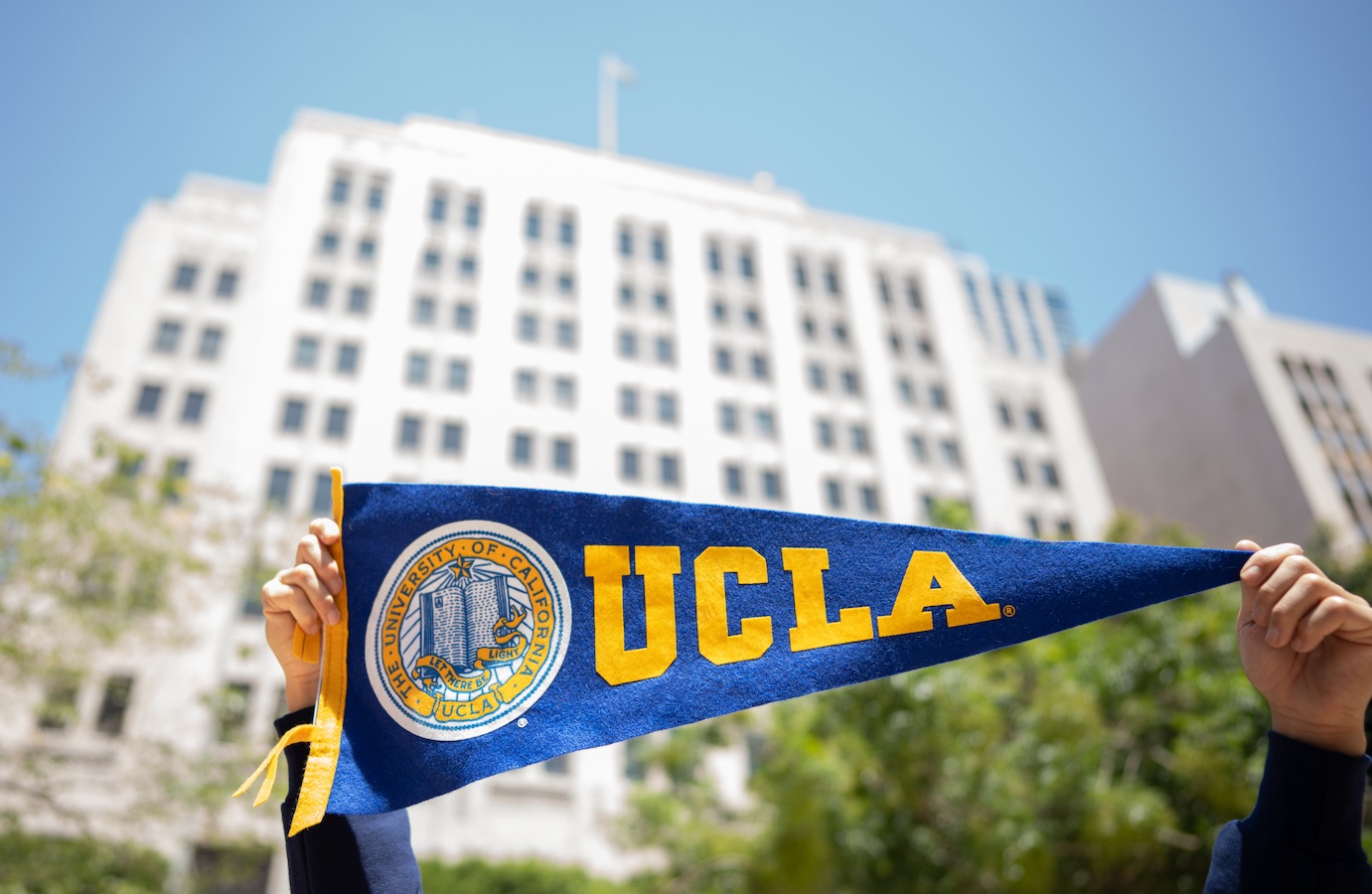 Hands holding UCLA pennant in front of dowtown Trust building